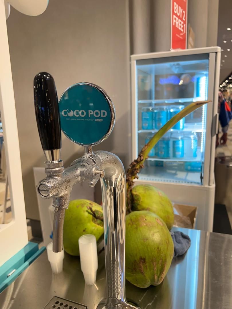Fresh green coconuts on a tap beside a Cocopod chiller at an in-store booth